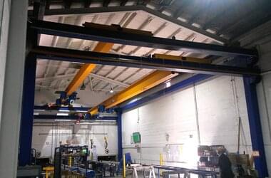 Single girder travelling crane at output stations of a long goods high-bay warehouse