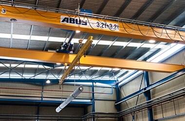 Double-girder travelling crane with spreader beam carries material for pipe production