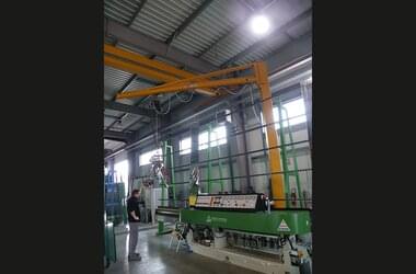 Employee working with pillar slewing jib crane in hall of Miroiterie Righetti company with single girder travelling crane