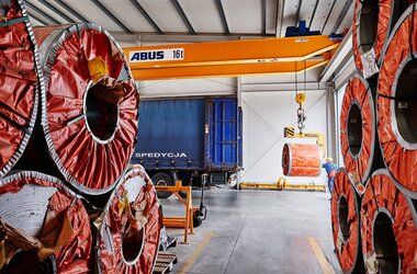 Double girder travelling crane loads steel coil into truck in logistics area