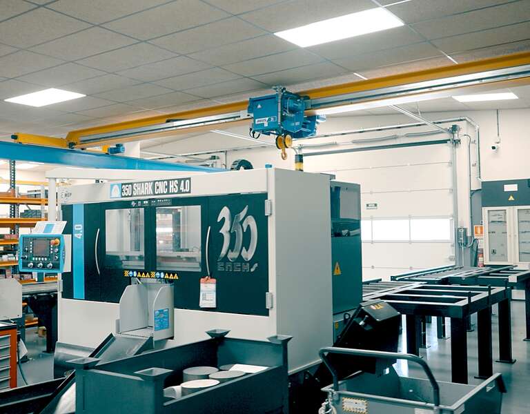 A factory floor with machine tools. An ELV bridge crane with electric wire rope hoist travels along a crane runway.