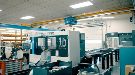 A factory floor with machine tools. An ELV bridge crane with electric wire rope hoist travels along a crane runway.
