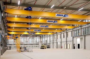 This view looks into a large production hall with five ELK cranes moving about on a crane track. On the second level, there are two semi-goliath cranes.
