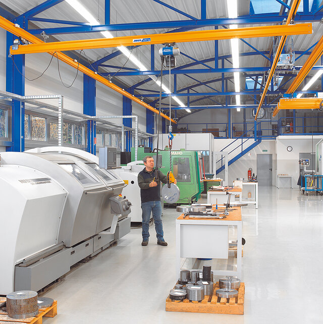 An employee operates a suspended rail system with a chain hoist and moves a load in a factory