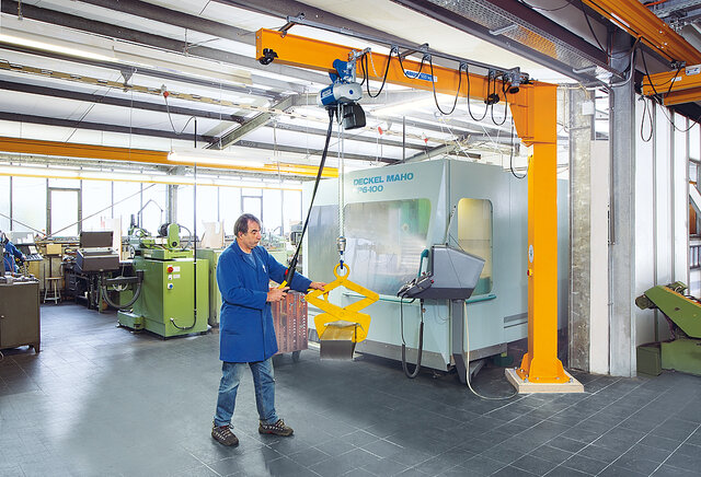 An employee operates a column-mounted jib crane and lifts a load using a chain hoist in a factory.