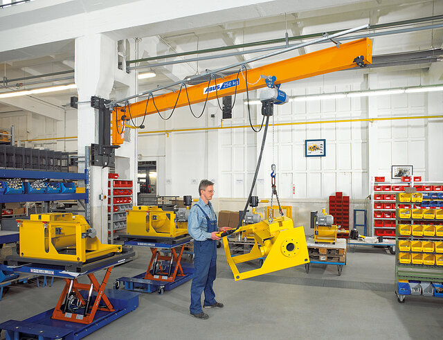 An employee operates a wall-mounted jib crane and moves a load using a chain hoist in a factory