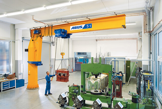 An employee operates a column-mounted jib crane and lifts a heavy load using a chain hoist in a factory